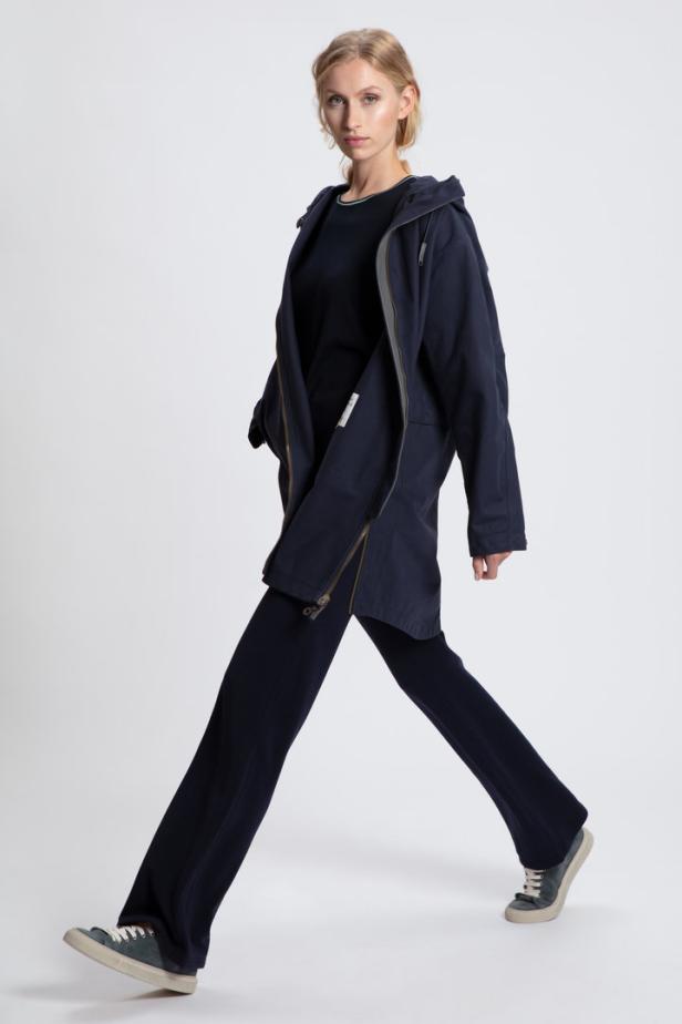 Eine Frau in marineblauer Jacke und Hose geht vor einem weißen Hintergrund.