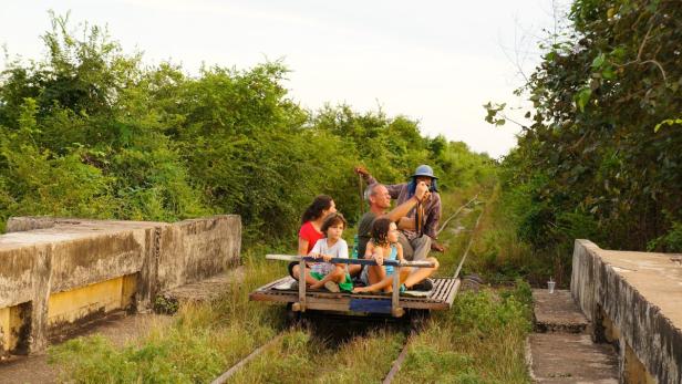 Eine Familie fährt mit einem Bambuszug durch die kambodschanische Landschaft.