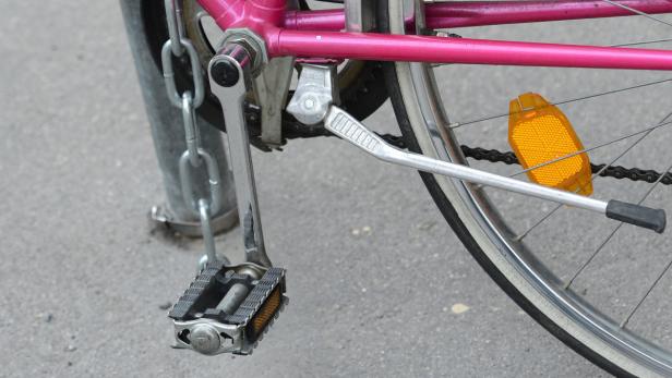 Ein pinkfarbenes Fahrrad ist mit einer Kette an einem Pfosten befestigt.