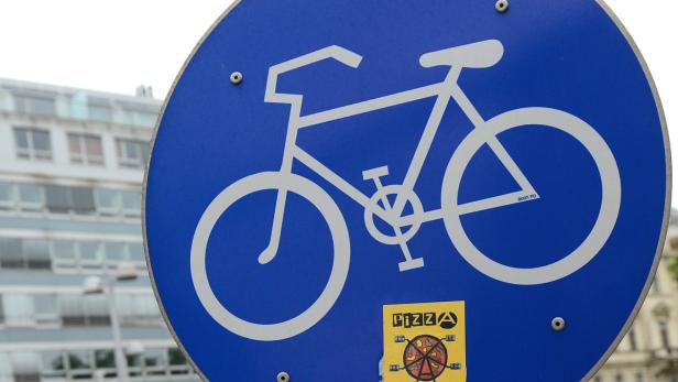 Ein blaues Verkehrsschild mit einem weißen Fahrradsymbol und einem Pizza-Aufkleber.