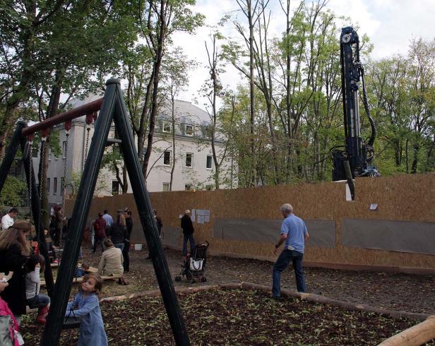 Auf einem Spielplatz spielen Kinder, während im Hintergrund eine Baumaschine steht.