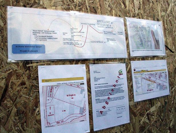 Mehrere Pläne und Dokumente zum Projekt „Hockepark“ der At.Home Immobilien GmbH hängen an einer Wand.
