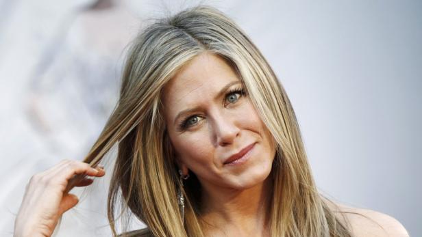 Jennifer Aniston lächelt und spielt mit einer Haarsträhne.