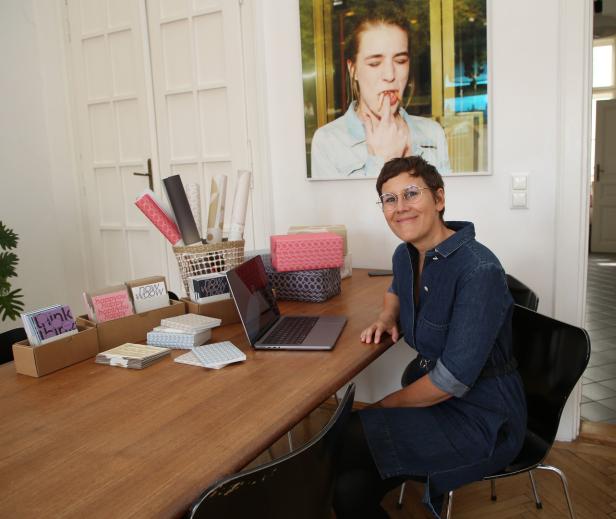 Eine Frau sitzt an einem Tisch mit einem Laptop und Geschenkpapierrollen.