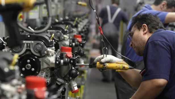 Ein Arbeiter montiert in einer Fabrik einen Motor mit einem gelben Schraubenschlüssel.