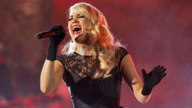Carrie Underwood singt während eines Auftritts in einem schwarzen Kleid und Handschuhen.