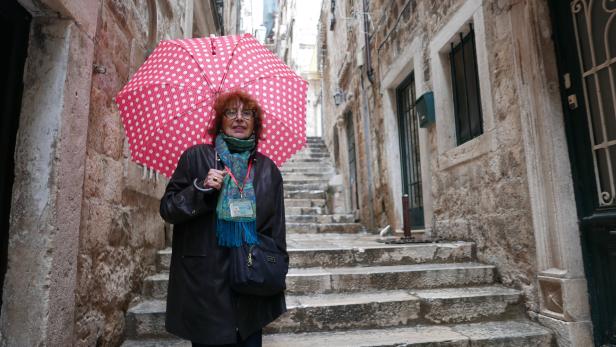 Eine Frau mit Regenschirm steht in einer Gasse mit Steintreppen.
