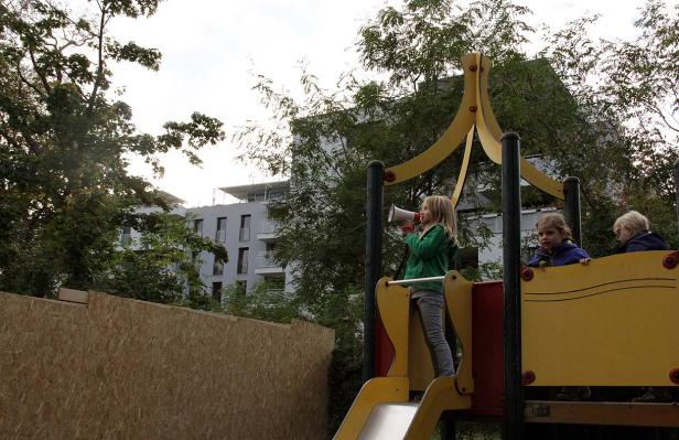 Ein Mädchen benutzt ein Megaphon auf einem Spielplatz, während andere Kinder zusehen.