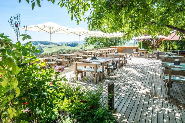 Einladende Terrasse eines Restaurants mit Blick auf eine grüne Hügellandschaft.