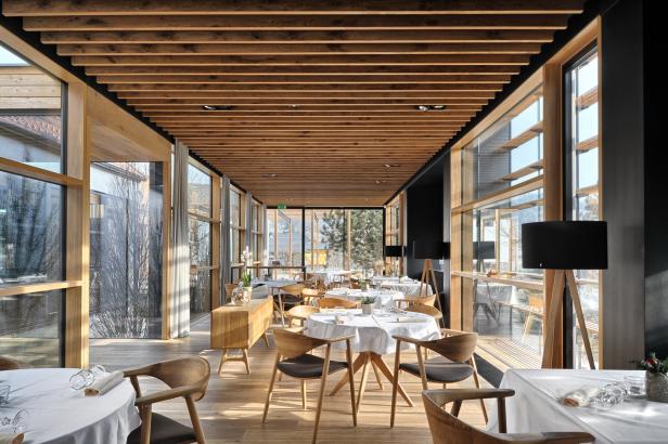 Ein helles Restaurant mit Holzbalkendecke und großen Fenstern mit Blick ins Freie.