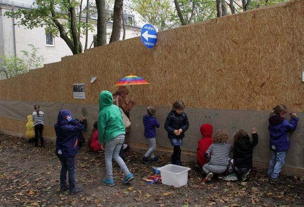 Kids, hockegasse Eine Gruppe Kinder malt auf einer langen Papierbahn an einer Holzwand im Freien.