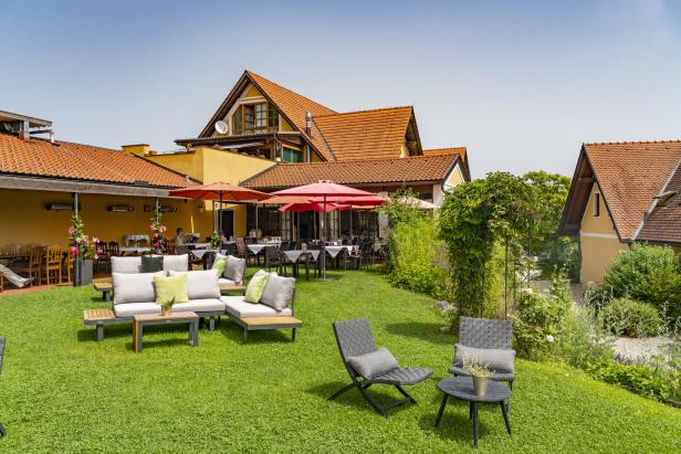 Ein Restaurantgarten mit Tischen, Stühlen und Loungemöbeln auf einem grünen Rasen.