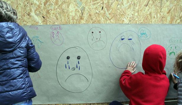 Kinder zeichnen traurige Gesichter auf ein großes Blatt Papier.