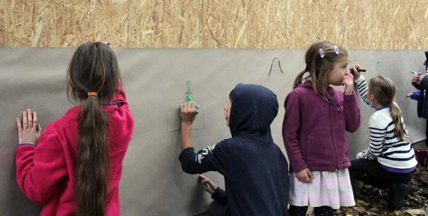 Eine Gruppe von Kindern malt mit Stiften auf eine große Papierwand.