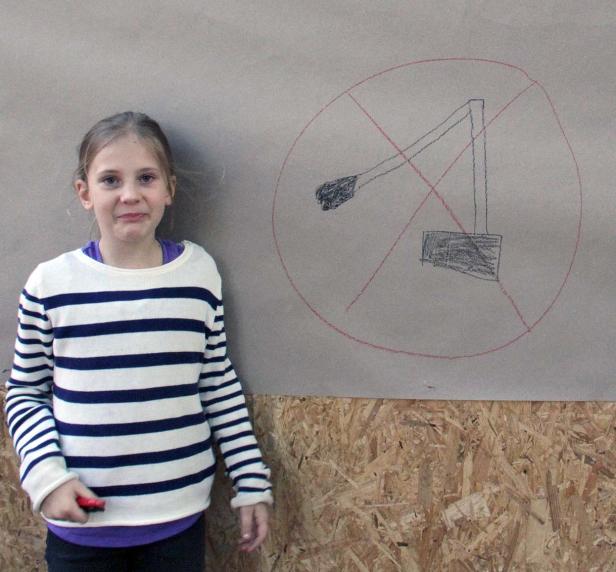 Ein Mädchen steht vor einem Plakat mit einem durchgestrichenen Kran.