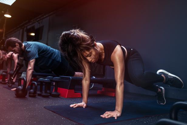 Eine Frau macht Liegestütze in einem Fitnessstudio, während andere trainieren.