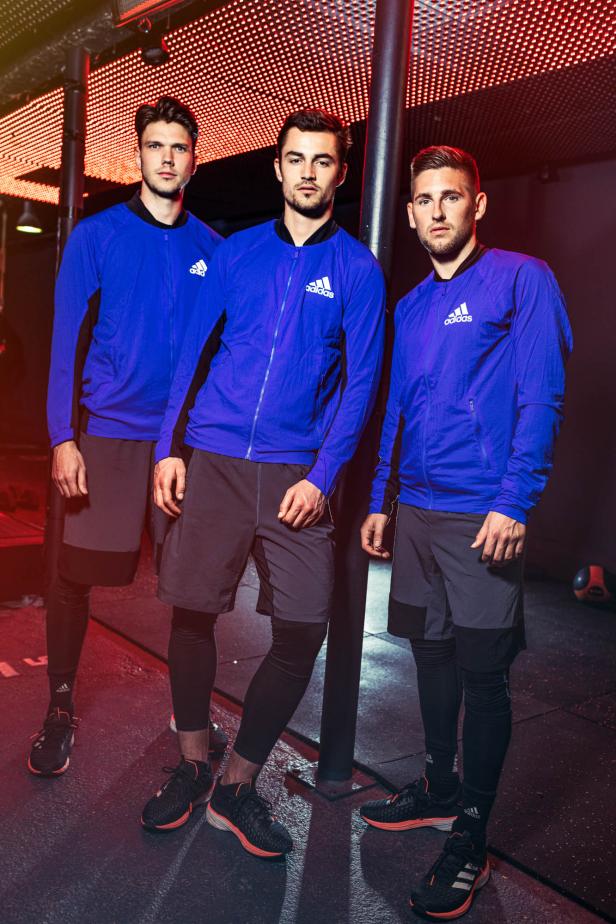 Drei Männer in blauen Adidas-Trainingsjacken und Shorts posieren für ein Foto.