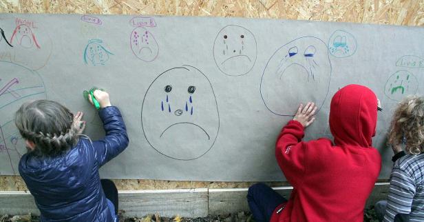 Kids, hockegasse Kinder zeichnen traurige Gesichter auf ein großes Blatt Papier.