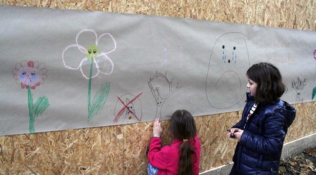 Zwei Mädchen betrachten eine Zeichnung mit traurigen Blumen und Bäumen auf einer Pappe.