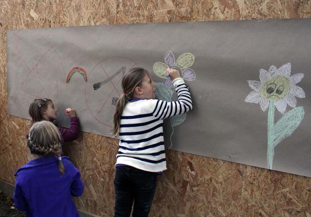 Kids, hockegasse Drei Mädchen malen mit Kreide auf einer großen Papierbahn an einer Holzwand.