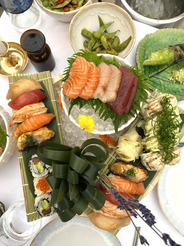 Eine Platte mit Sushi, Sashimi und Edamame auf einem weißen Tisch angerichtet.