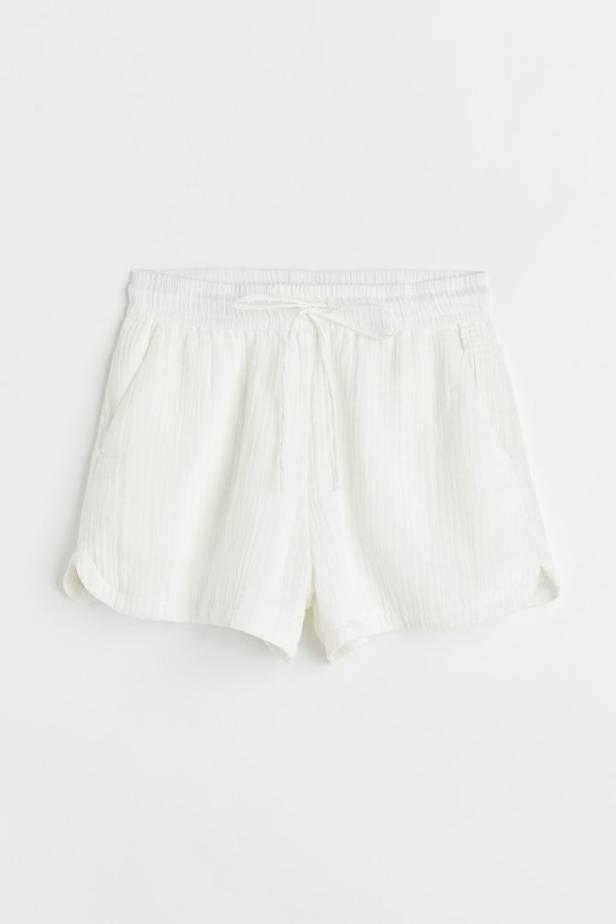 Eine weiße, kurze Stoffhose mit Kordelzug liegt vor einem weißen Hintergrund.