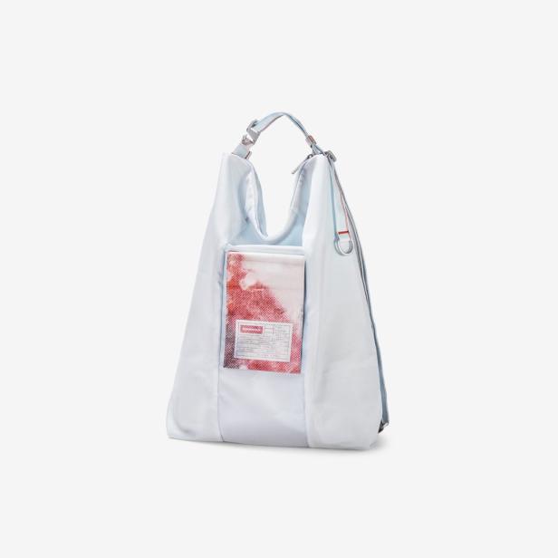 Eine hellblaue Stofftasche mit einem Fach, in dem ein Etikett mit rotem Muster steckt.