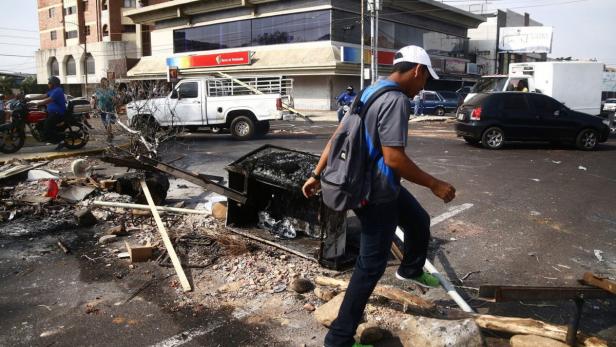 Ein Mann überquert eine Straße voller Trümmer und Müll in einer städtischen Umgebung.