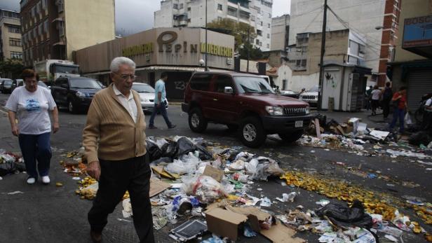 Ein älteres Paar geht über eine Straße voller Müll in einer städtischen Umgebung.