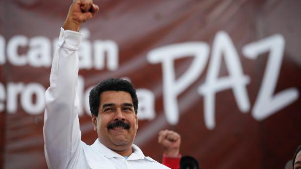 Nicolás Maduro mit erhobener Faust vor einem Banner mit der Aufschrift „PAZ“ (Frieden).