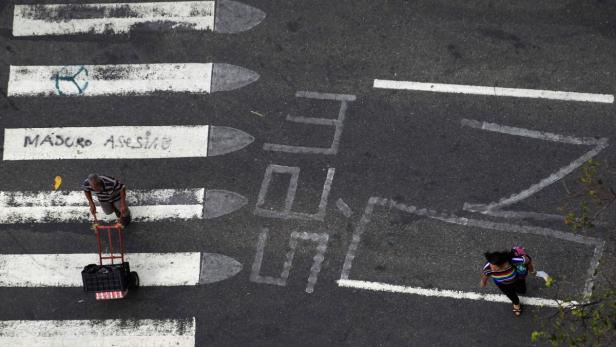 Ein Mann zieht einen Wagen über einen Zebrastreifen mit der Aufschrift „Maduro Asesino“.