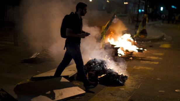 Ein Mann geht nachts an einem brennenden Barrikade vorbei.