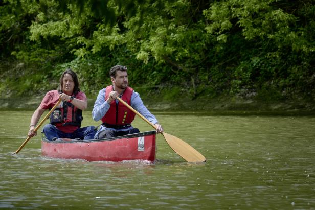 Zwei Männer paddeln in einem roten Kanu auf einem Fluss.