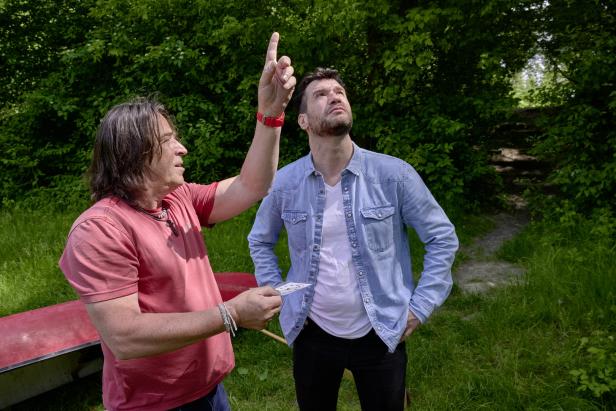 Zwei Männer stehen im Grünen, einer zeigt mit dem Finger nach oben.
