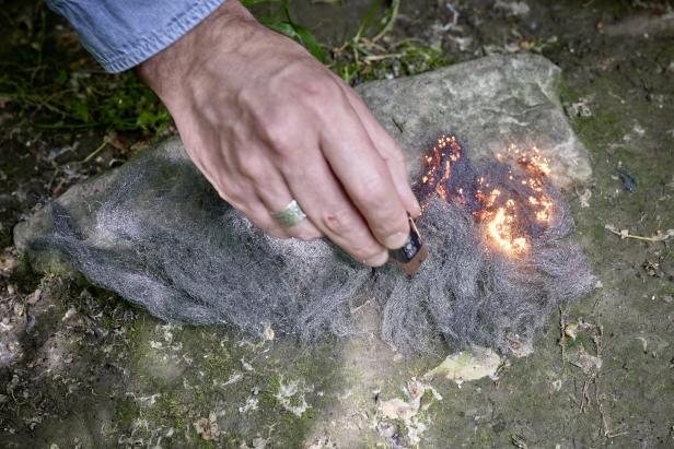 Eine Hand entzündet mit einer Batterie Stahlwolle, um ein Feuer zu starten.