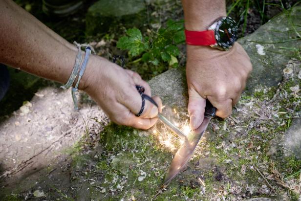 Eine Person entzündet mit einem Messer und einem Feuerstahl ein Feuer.