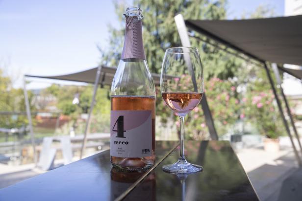 Eine Flasche und ein Glas Rosé Secco stehen auf einem Tisch im Freien.