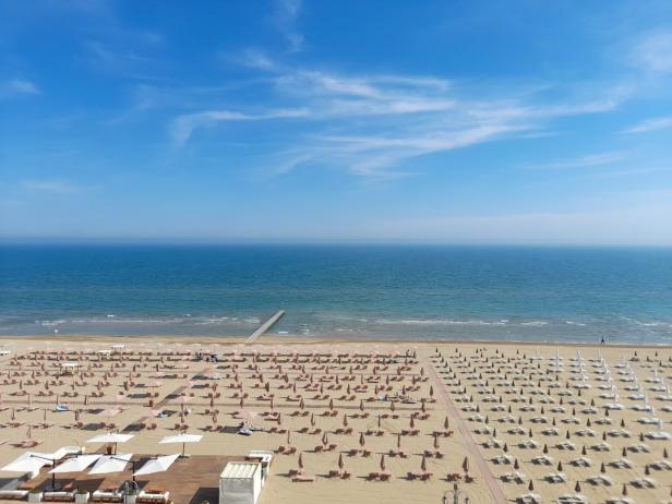 Luftaufnahme eines Strandes mit vielen Sonnenschirmen und Liegestühlen am Meer.