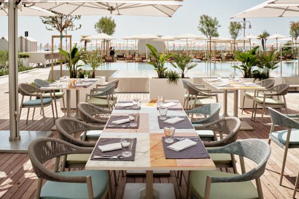 Ein gedeckter Tisch in einem Restaurant im Freien mit Blick auf einen Pool und den Strand.