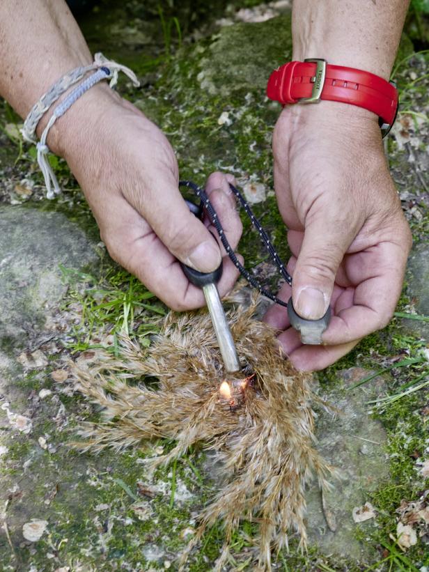 Eine Person entzündet mit einem Feuerstahl ein kleines Feuer.