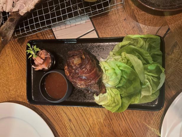 Ein Schweinshaxe mit Salat, Sauce und Beilagen auf einem schwarzen Teller.