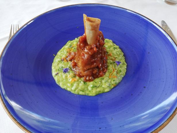 Ossobuco auf einem Bett aus grünem Risotto, serviert auf einem blauen Teller.