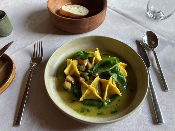 Ein Teller Tortelloni mit Pilzen, Erbsen und Basilikum in einer hellen Soße.