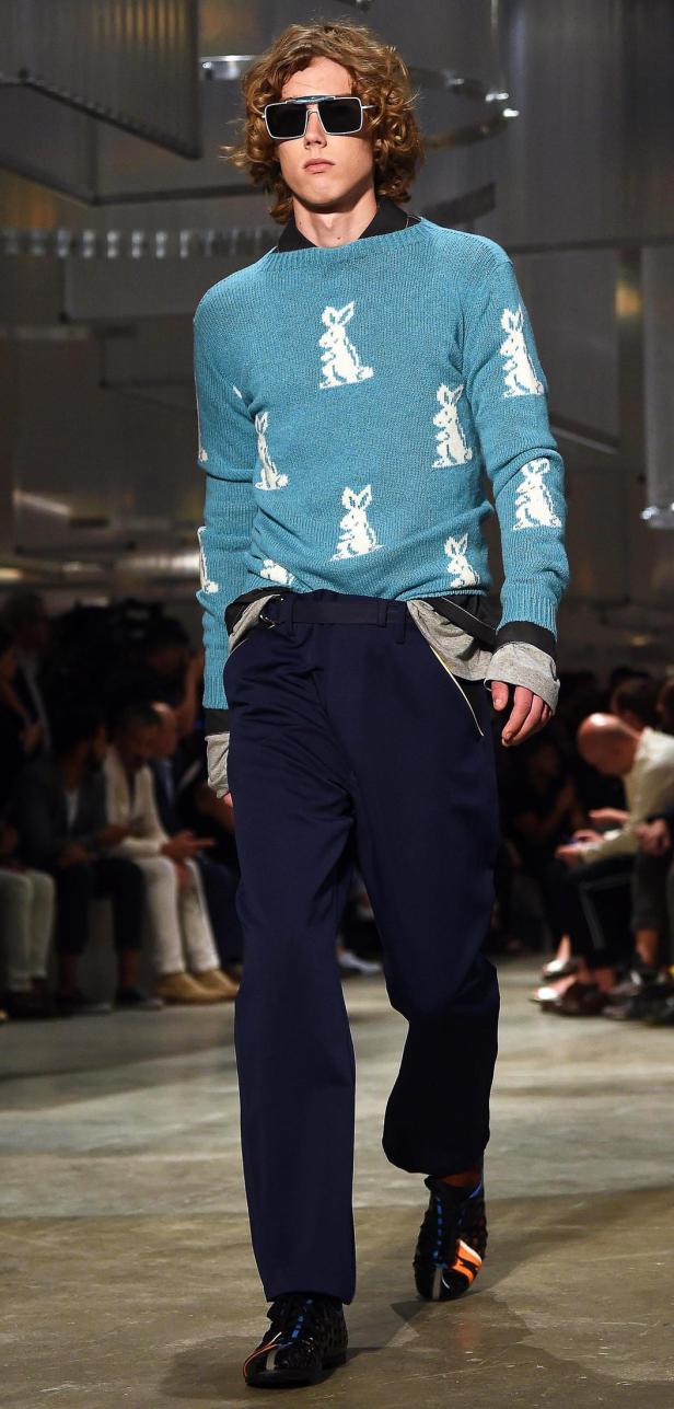 Ein Mann mit Sonnenbrille und blauem Pullover mit Hasenmuster läuft über einen Laufsteg.