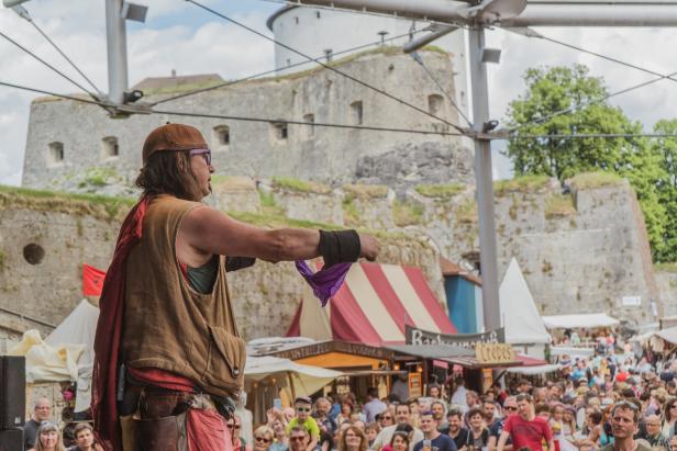 Ein Mann in historischer Kleidung führt auf einem Mittelaltermarkt ein Zaubertrick vor.