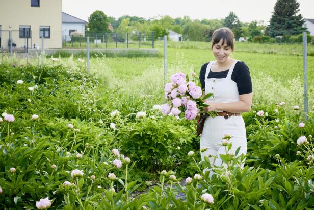 Eine Frau steht in einem Feld voller Pfingstrosen und hält einen Strauß in den Händen.