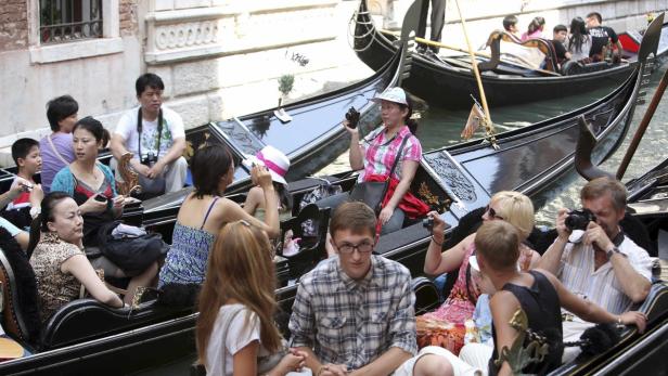 Touristen fahren in Gondeln durch die Kanäle von Venedig und fotografieren.