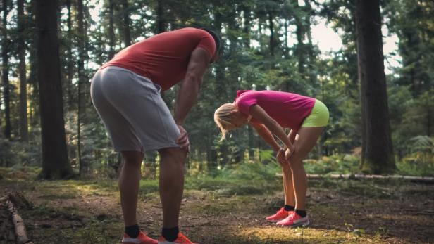 Ein Mann und eine Frau machen eine Pause beim Joggen im Wald.