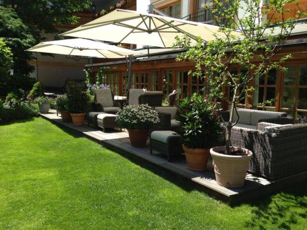 Eine Terrasse mit Gartenmöbeln und Sonnenschirmen grenzt an einen gepflegten Rasen.