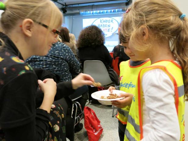 Zwei Kinder in Warnwesten bekommen Kekse von einer Frau.